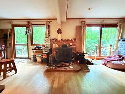 部屋の中心に佇むレンガの薪ストーブが主役のリビング。左右の大きな木製サッシ窓からは、豊かな森がパノラマで広がります。冬は暖炉の火を眺め、夏は緑の特等席となる、暮らしを彩るシンボル空間です。
