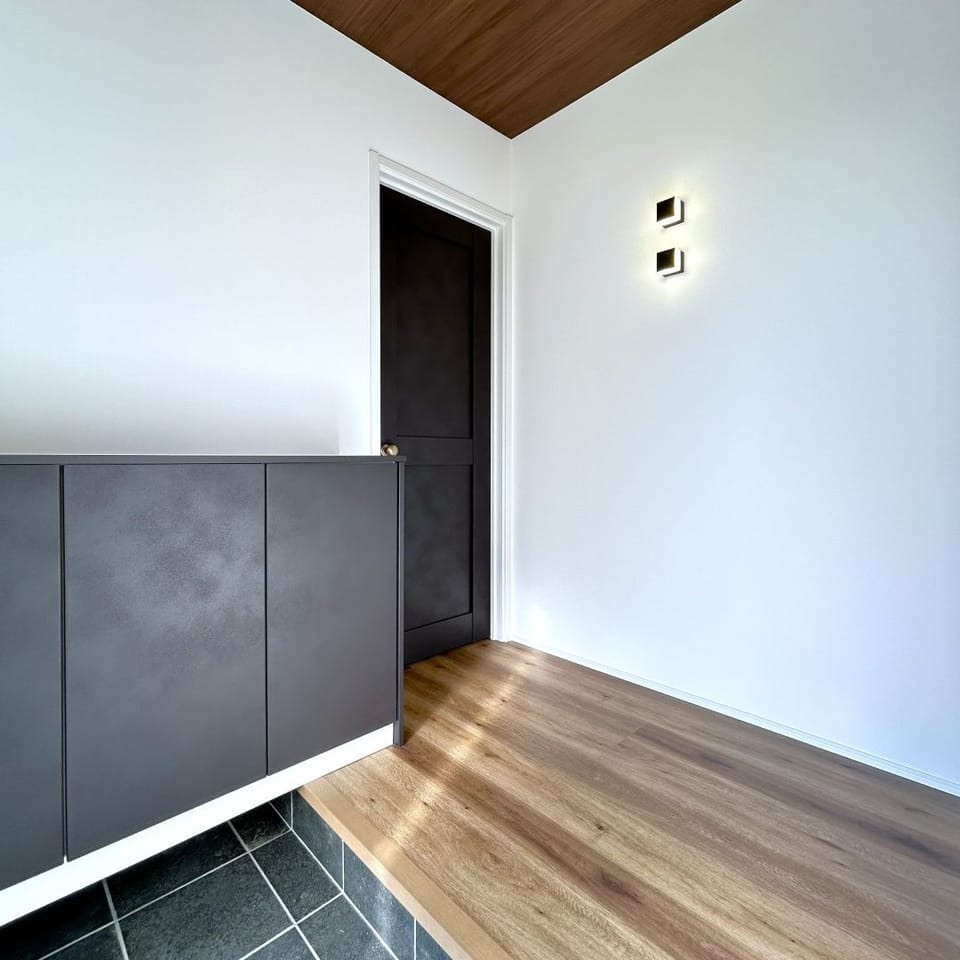 木目柄の天井とチャコールブラックのシューズボックスが、モダンな印象を与える玄関ホール。