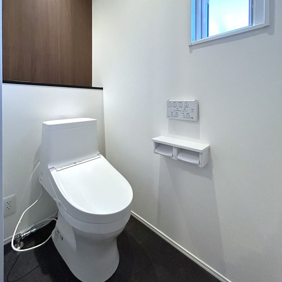 ブラック×ホワイトの洗練空間に、木目クロスが温もりを添える上質なトイレ。デザイン性と落ち着きを両立。