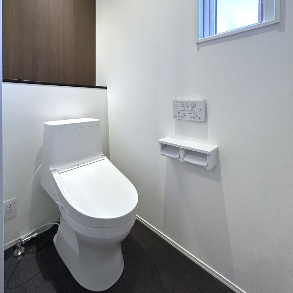 ブラック×ホワイトの洗練空間に、木目クロスが温もりを添える上質なトイレ。デザイン性と落ち着きを両立。