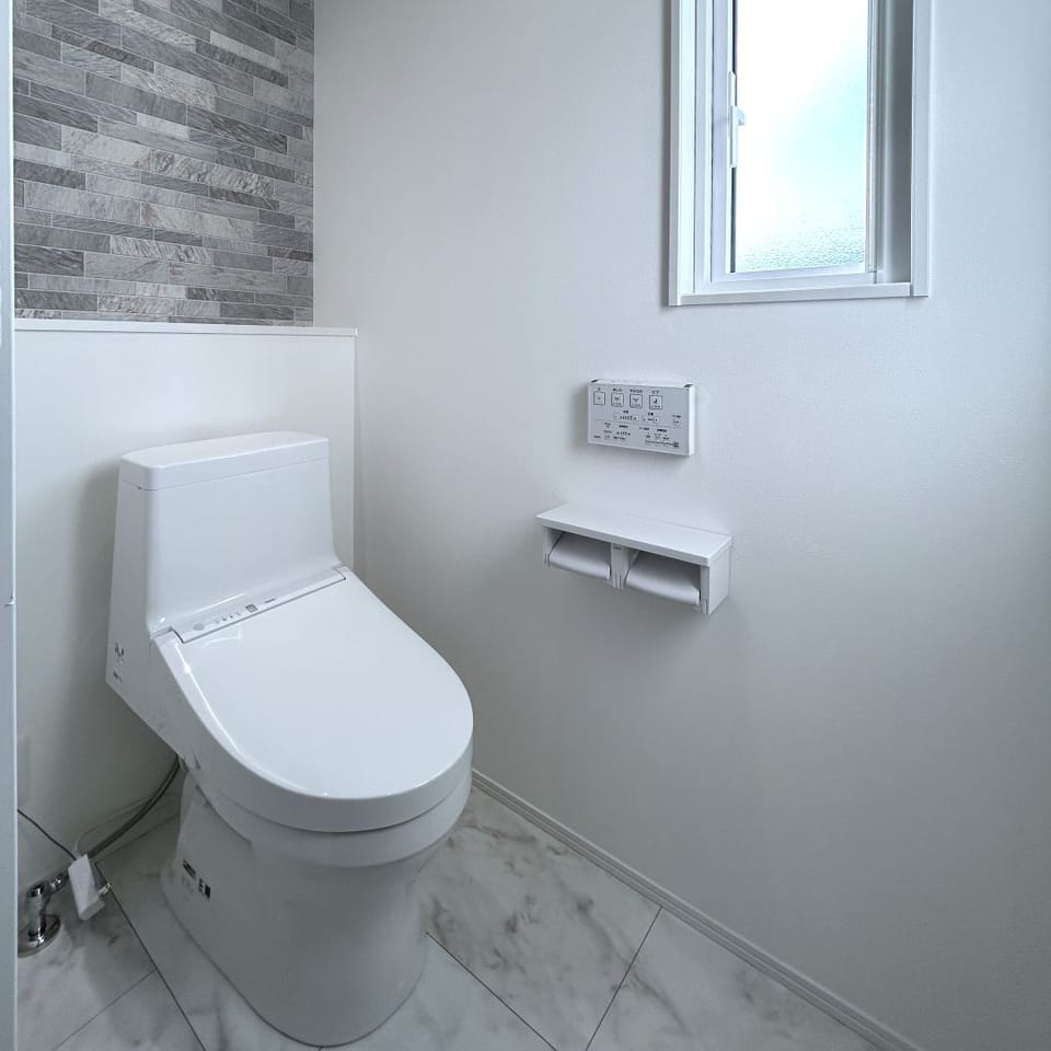 TOTO製トイレを採用した、清潔感のある空間。天然石の風合いを表現したタイル柄アクセントクロスで、落ち着いた印象に。