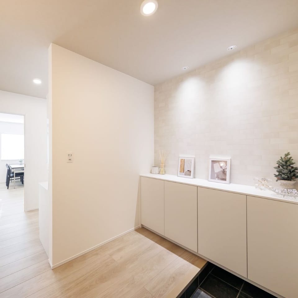 ホワイト×グレージュでナチュラルにコーディネートした、広々玄関ホール。ほっと和らぐ照明使いもポイント。